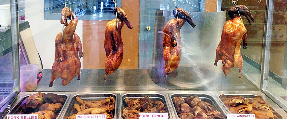 Roast ducks hanging above trays of pork belly and other BBQ